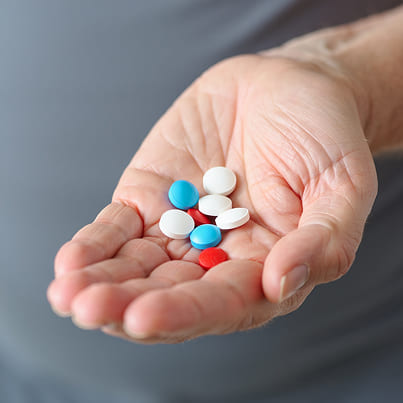 Рука держит множество разных таблеток и пилюль